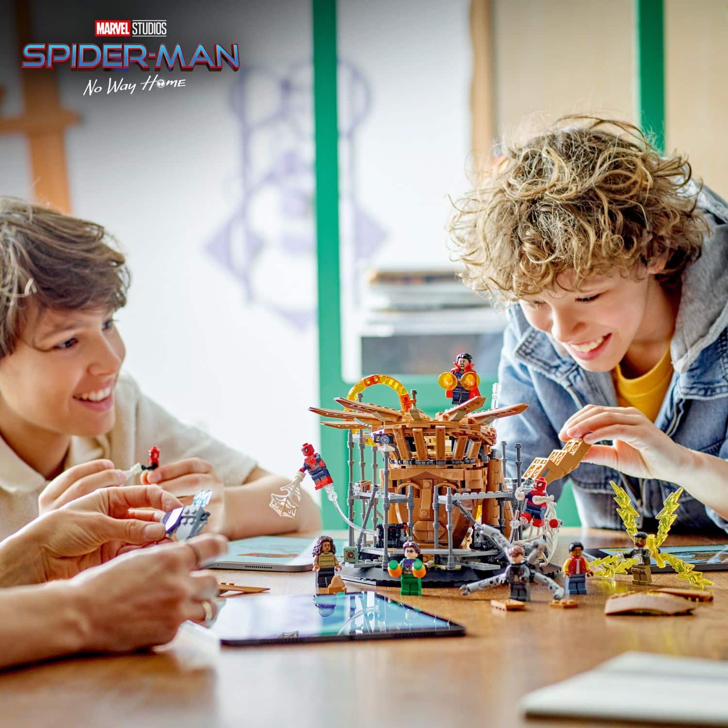 The image features two young boys playing with a toy building set, likely a Lego set, on a table. They are surrounded by various toys and building blocks, which they are actively engaged in constructing and enjoying. The boys are smiling and having fun, which suggests that they are enjoying their time together and the creative process of building with the toys.