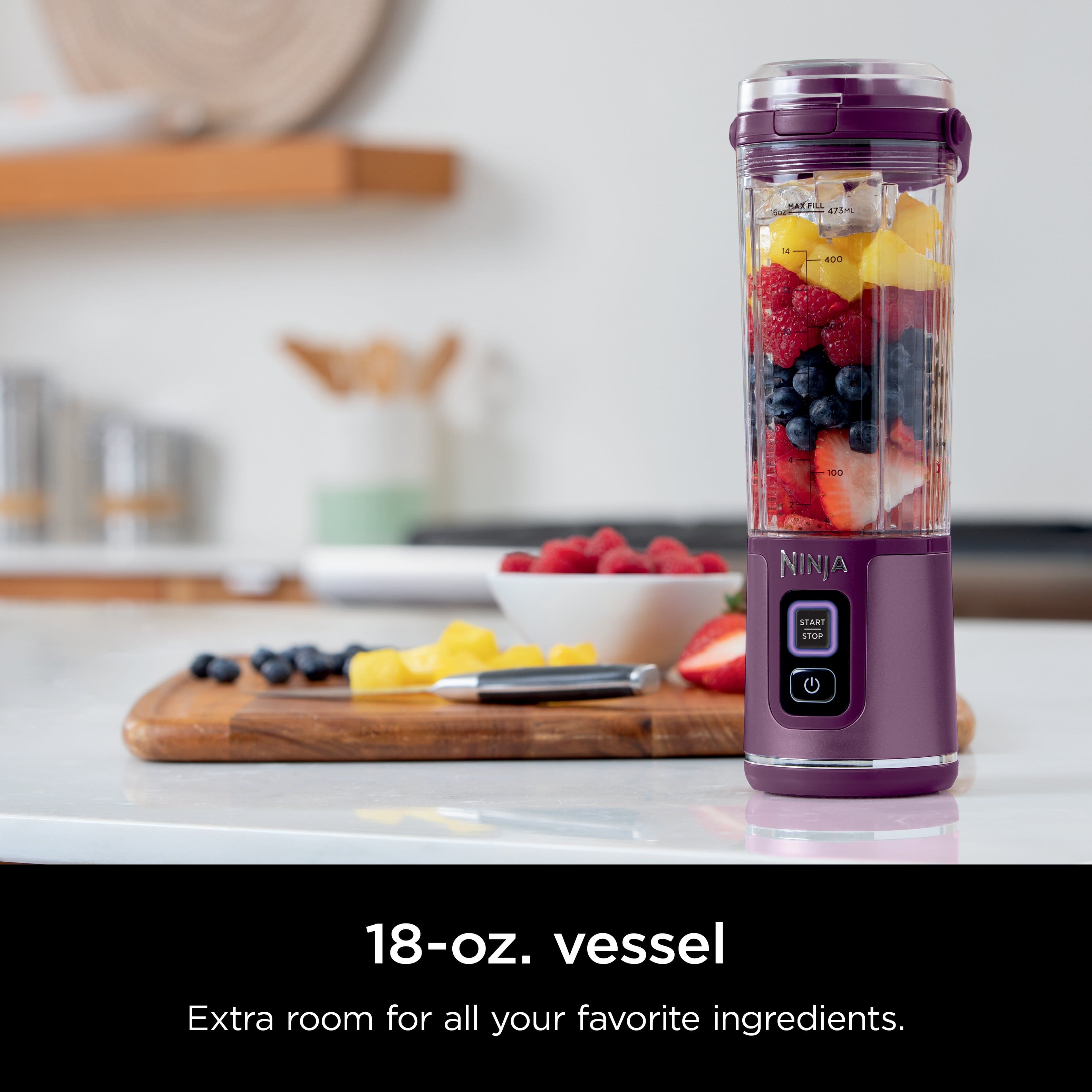 The image features a Ninja blender filled with various fruits, including strawberries, blueberries, and raspberries. The blender is placed on a counter, and there is a bowl of fruit nearby. The blender is designed to hold 18 ounces of ingredients, providing ample space for your favorite ingredients.