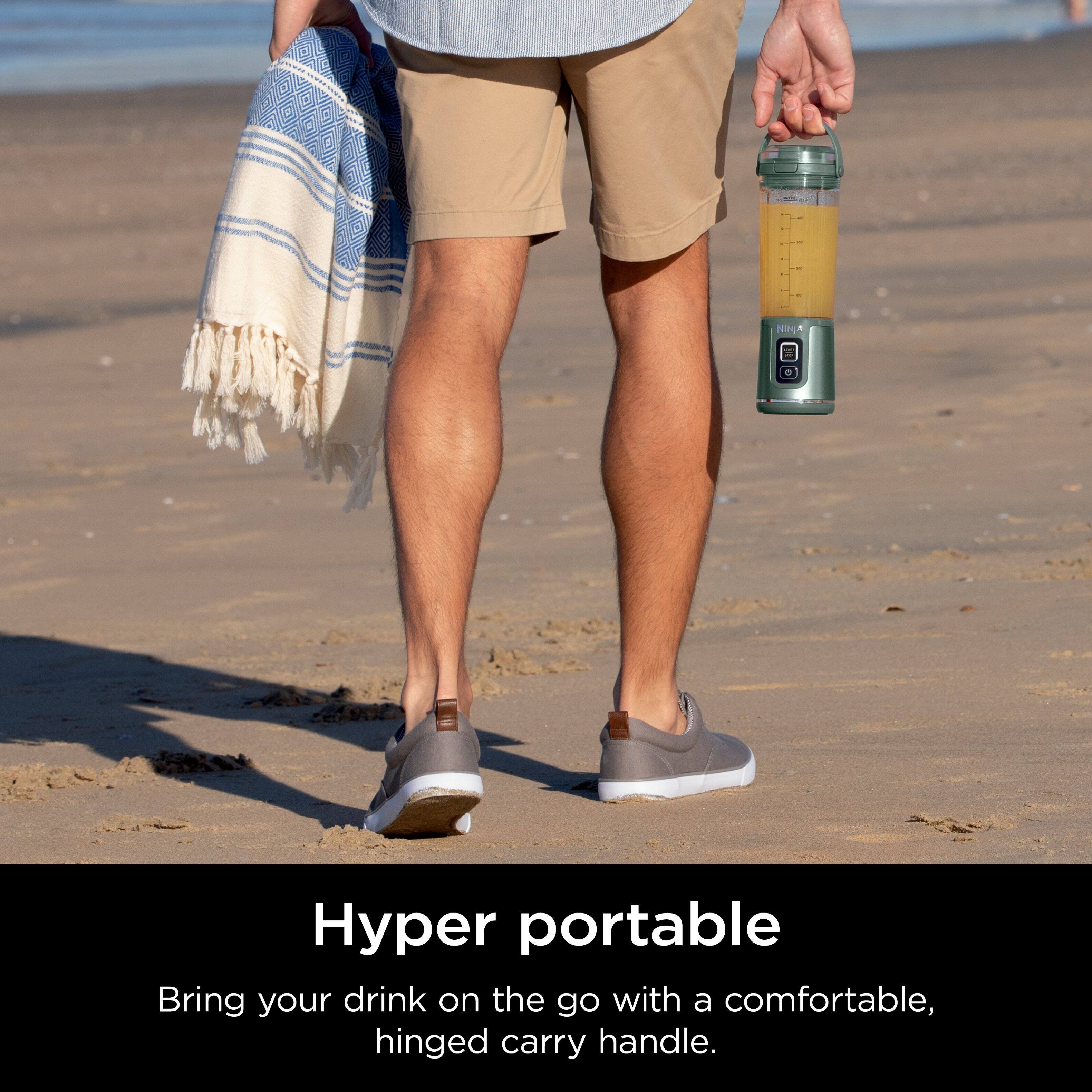The image features a man walking on a beach while holding a water bottle in his hand. The water bottle has a hinged carry handle, making it convenient for the man to carry it while walking. The man is also holding a towel, which suggests that he might be enjoying a day at the beach. The scene conveys a sense of relaxation and leisure, as the man is able to carry his drink and towel with ease.