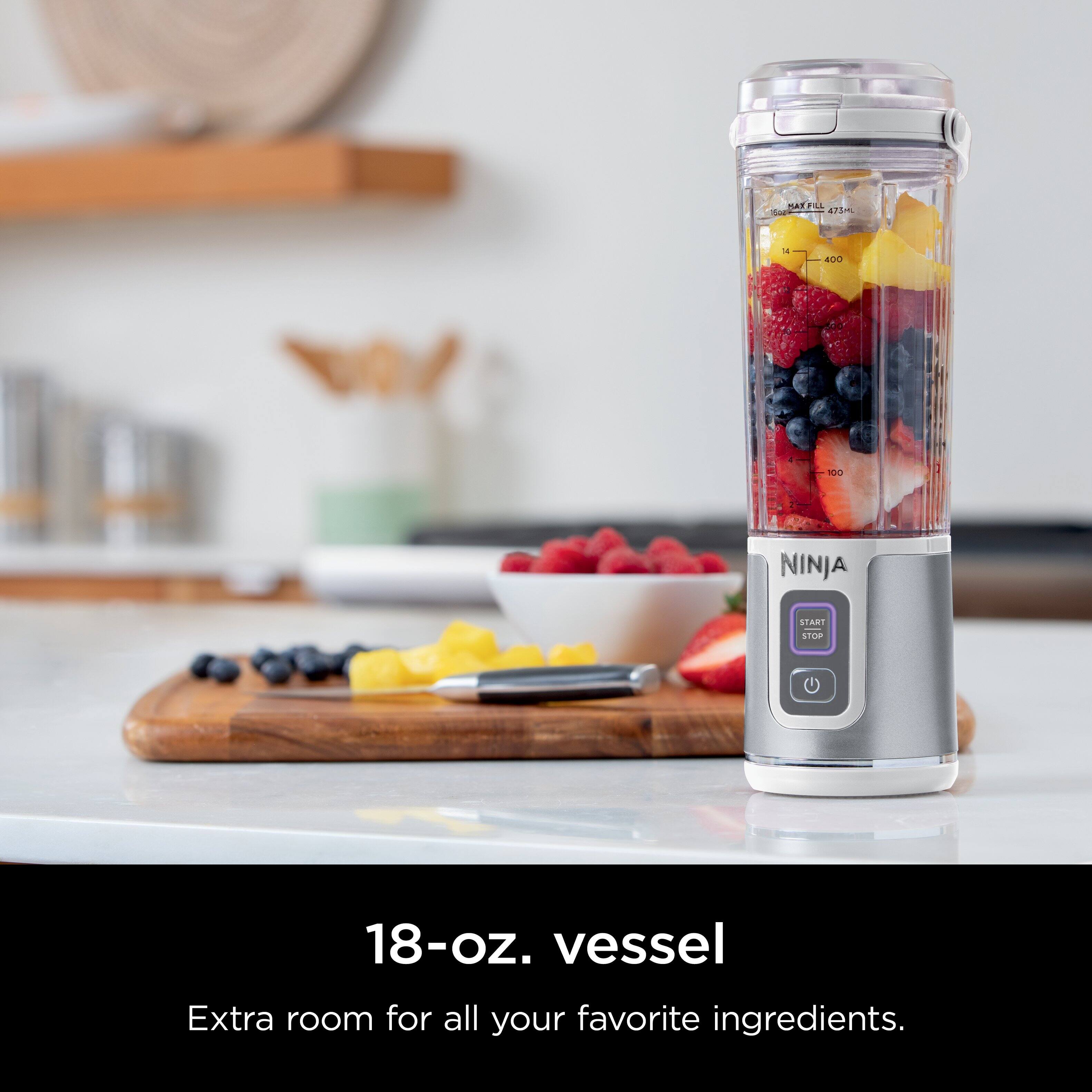 The image features a Ninja Nutri-Blender with a 18-oz. vessel, which is filled with various fruits and ingredients. The blender is placed on a countertop, surrounded by a bowl of fruit and a cutting board. The blender is designed to provide extra room for all your favorite ingredients, making it a versatile and convenient appliance for preparing smoothies and other blended beverages.