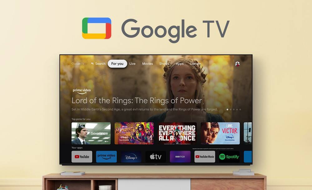 The image features a large flat screen TV displaying the Google TV homepage. The TV screen showcases various options, such as live movies, shows, and apps, as well as a library section. The homepage is promoting the Lord of the Rings: The Rings of Power, a popular TV series set in Middle Earth's Second Age. The TV screen also displays the top picks for users, including Marvel's Severance, Disney+, and other popular shows and movies.