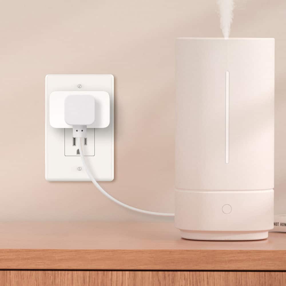 The image shows a white appliance plugged into an outlet on a wooden counter. The appliance appears to be a humidifier or an air purifier, as it is designed to improve the air quality in a room. The appliance is connected to the outlet via a cord, which is plugged into the wall socket. The scene suggests that the appliance is being used to enhance the indoor environment, possibly by adding moisture to the air or filtering out pollutants.