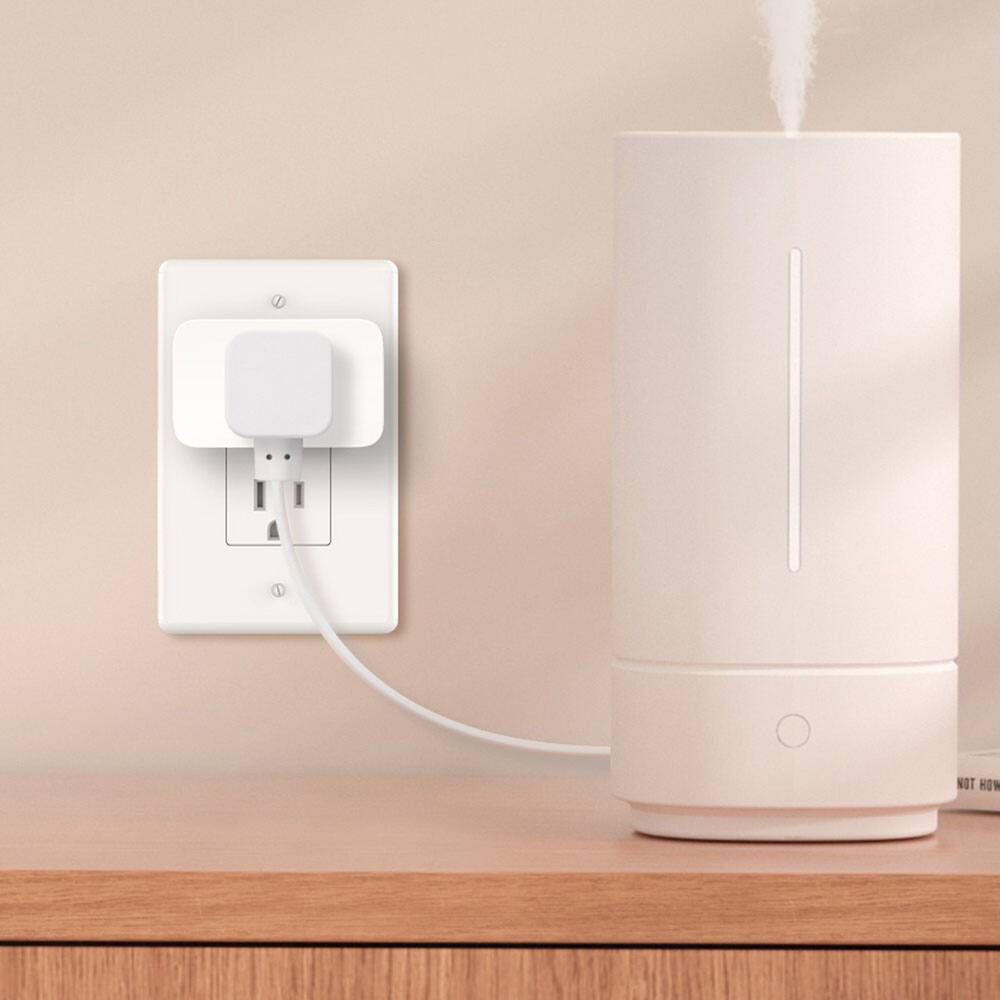 The image shows a white appliance plugged into an outlet on a wooden counter. The appliance appears to be a humidifier or an air purifier, as it is designed to improve the air quality in a room. The appliance is connected to the outlet via a cord, which is plugged into the wall socket. The scene suggests that the appliance is being used to enhance the indoor environment, possibly by adding moisture to the air or filtering out pollutants.