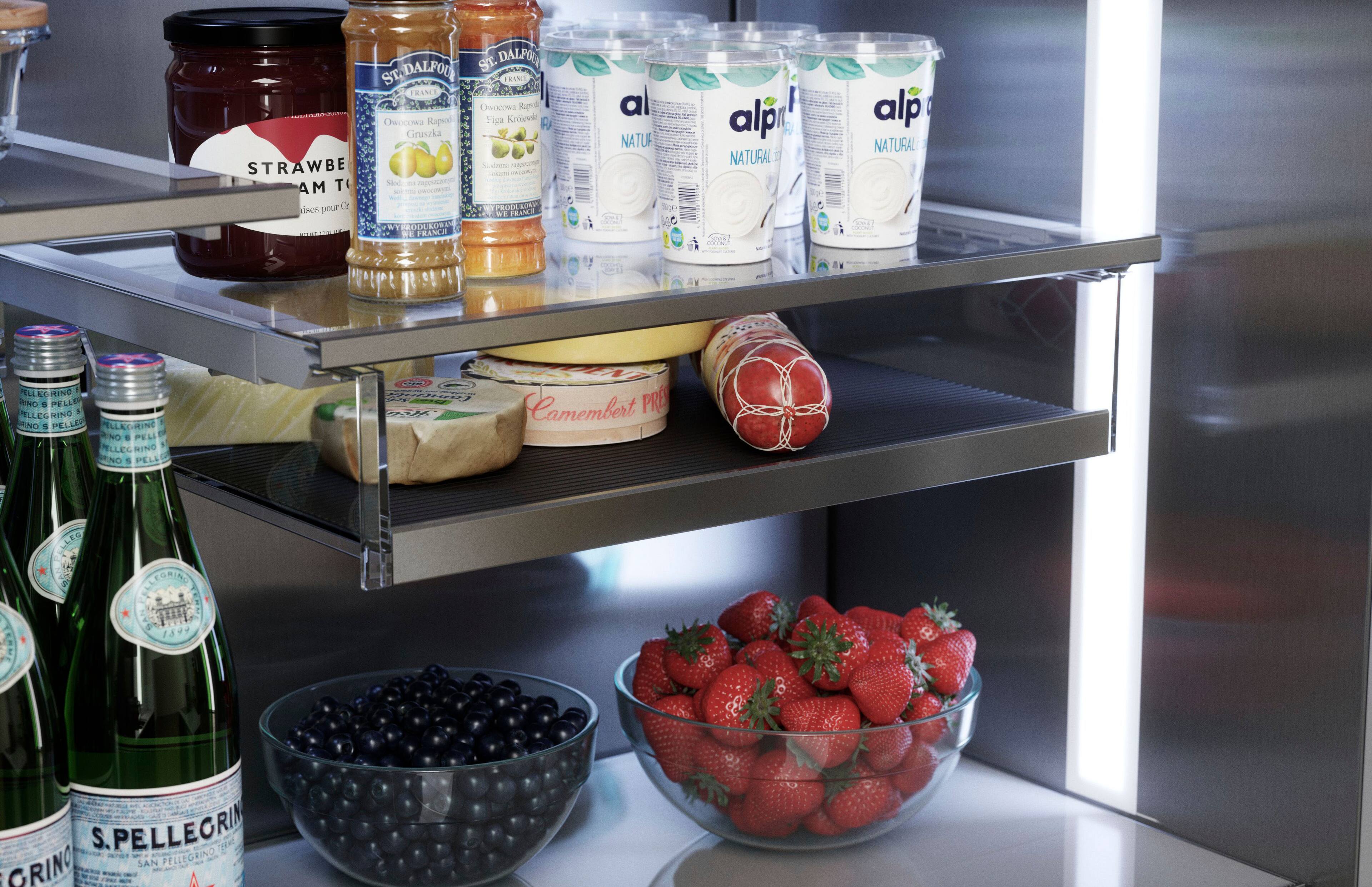 The image shows a refrigerator with a variety of food items and drinks. There are several bottles, including a bottle of wine, and a bowl of fruit, which contains strawberries. The refrigerator also has a shelf with a variety of food items, such as cheese and yogurt. The refrigerator is filled with different types of food and drinks, making it a well-stocked and organized space.