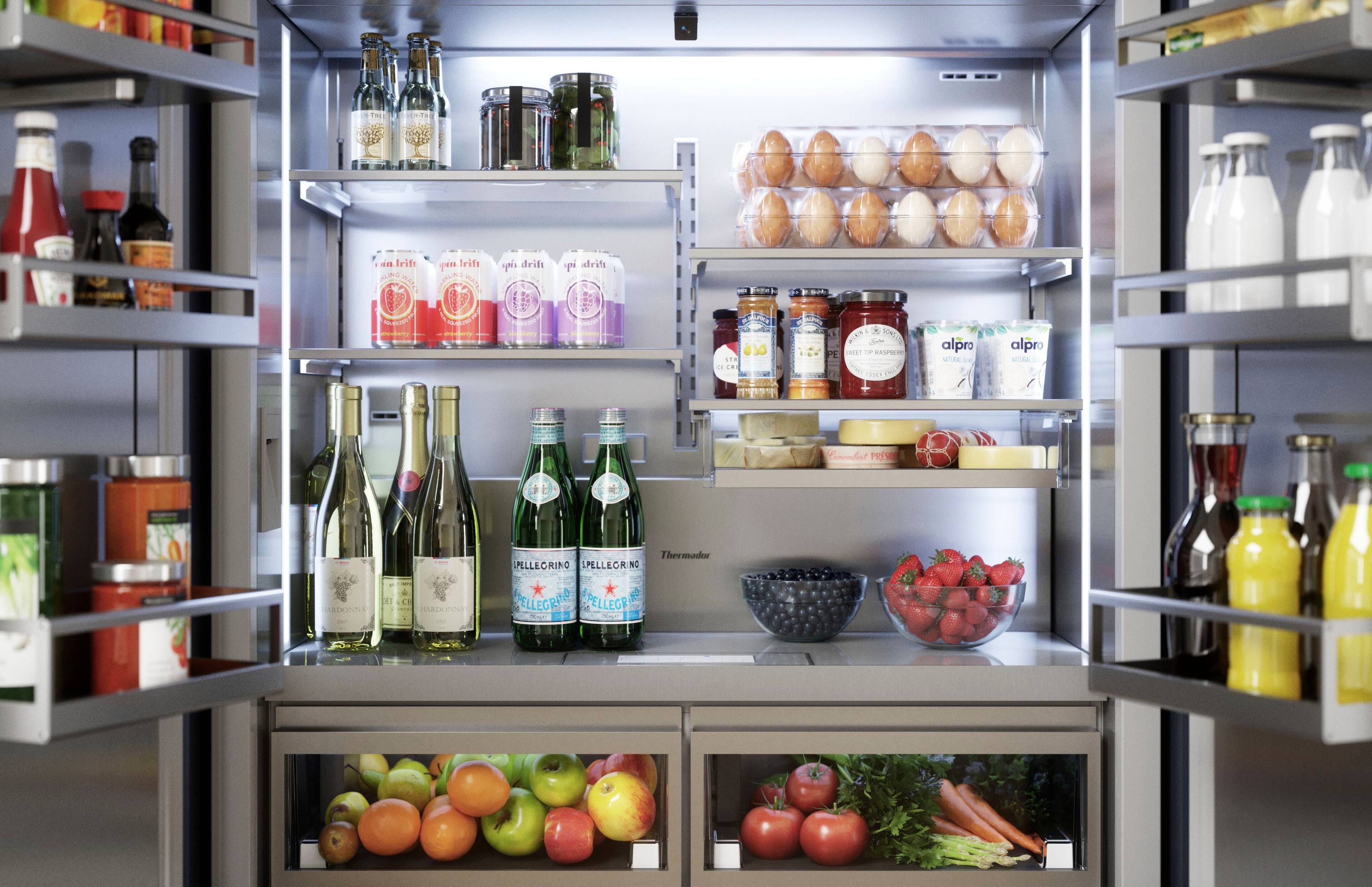 The image features a refrigerator filled with various food items and drinks. There are several bottles of wine and other beverages, as well as a bowl of fruit, including apples and oranges. The refrigerator also contains a variety of condiments and other food items, such as carrots and broccoli. The assortment of items in the refrigerator suggests that it is well-stocked and ready for use.