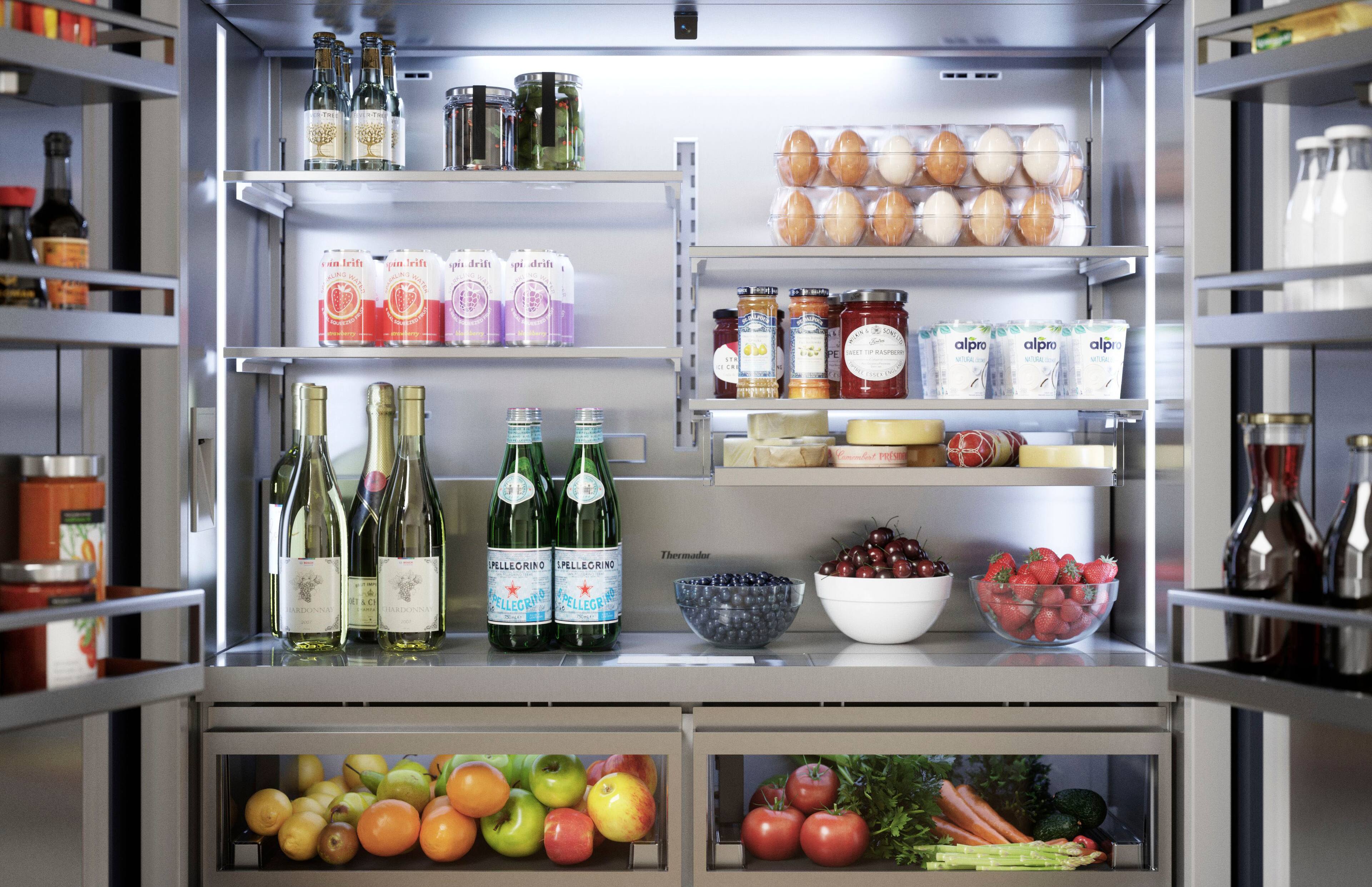 The image shows a refrigerator filled with a variety of food items. On the shelves, there are several bottles of wine, including a bottle of Pellegrino. The refrigerator also contains a bowl of fruit, including apples and oranges, as well as a bowl of berries. There are also multiple carrots stored in the refrigerator. The refrigerator is well-stocked with a diverse assortment of food items, making it a convenient and healthy option for meal preparation.