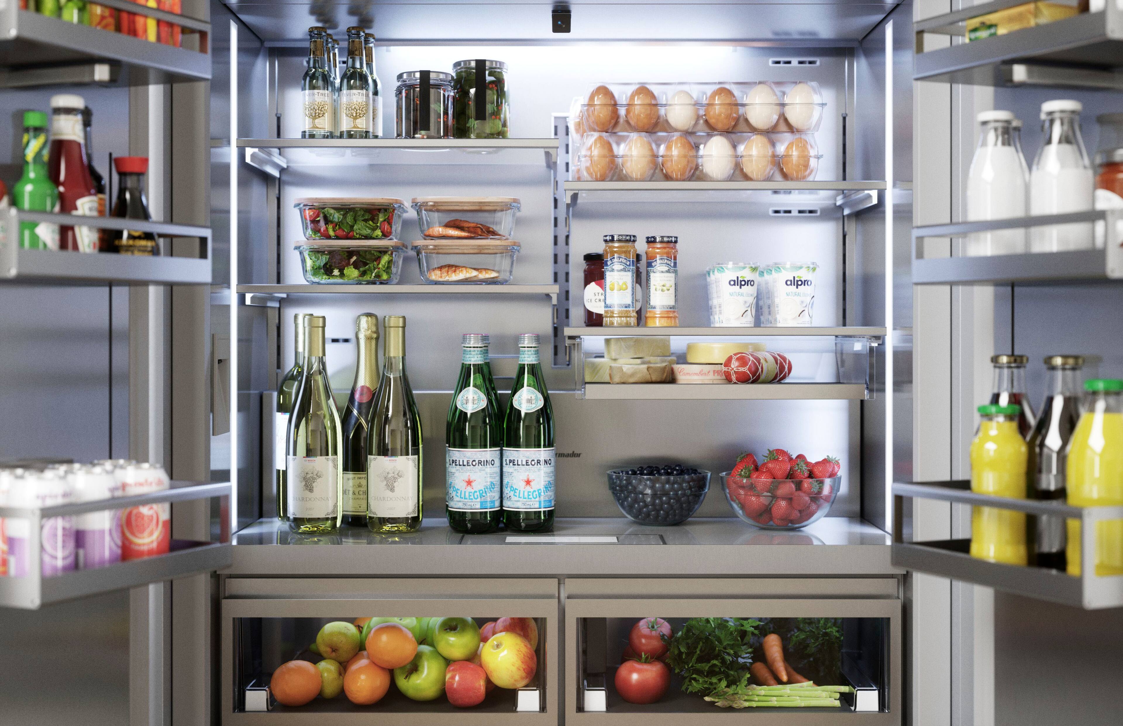 The refrigerator is filled with various food items and drinks. There are multiple bottles of wine, including a bottle of Pellegrino, and other beverages such as juice. The refrigerator also contains a bowl of fruit, including apples and oranges, as well as a bowl of vegetables. Additionally, there are eggs and other food items stored in the refrigerator. The refrigerator is well-stocked with a variety of items to choose from.