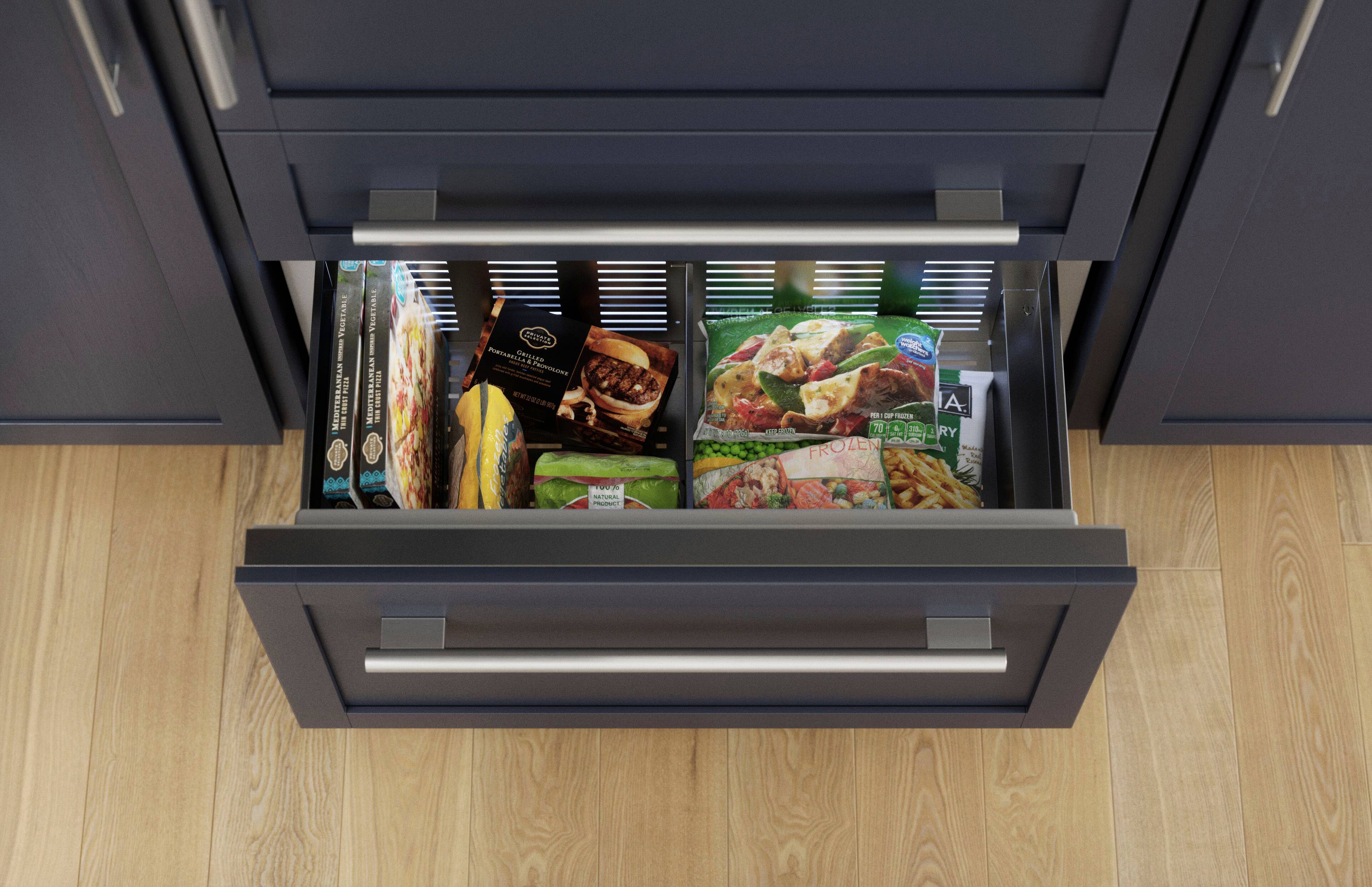 The image shows a drawer in a kitchen, filled with various food items. The drawer contains a variety of snacks, including a pizza, a sandwich, and some vegetables. The pizza is placed towards the back of the drawer, while the sandwich is located in the middle. The vegetables are scattered throughout the drawer, with some placed near the front and others near the back. The drawer is open, revealing the assortment of food items stored inside.