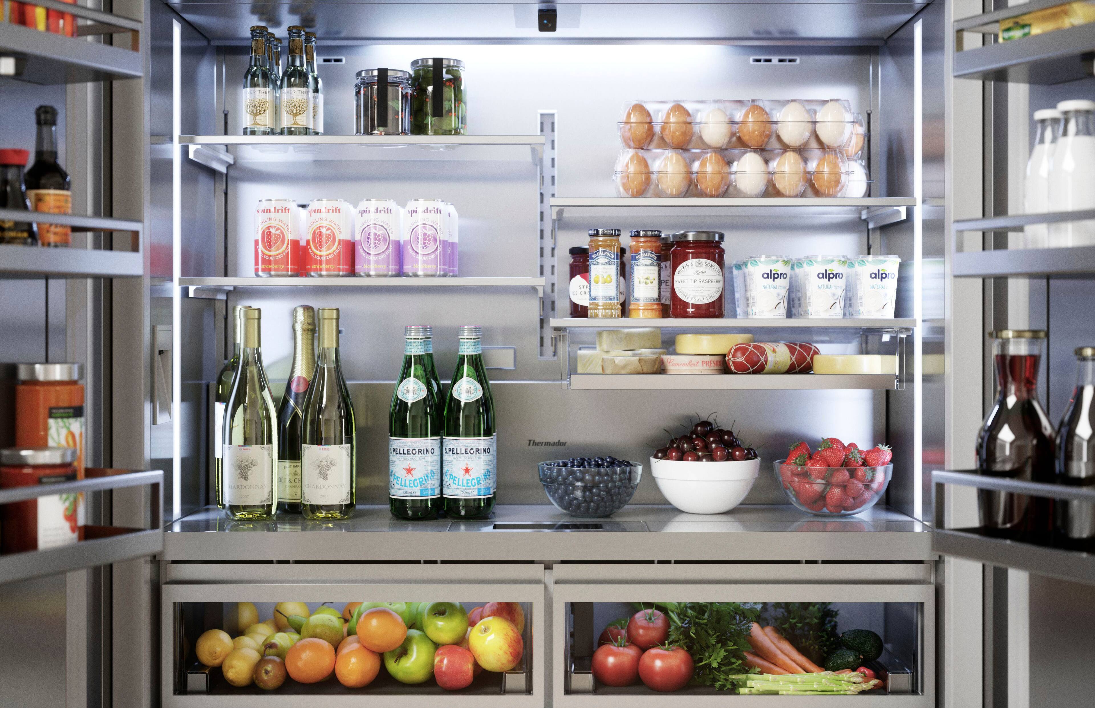 The refrigerator is stocked with a variety of food items and drinks. There are several bottles of wine, including Pellegrino and Chardonnay, as well as other drinks such as alpro and thermos. The refrigerator also contains a bowl of fruit, including apples and oranges, and a bowl of vegetables. Additionally, there are eggs and other food items stored in the refrigerator. The refrigerator is well-organized and offers a diverse selection of items for consumption.