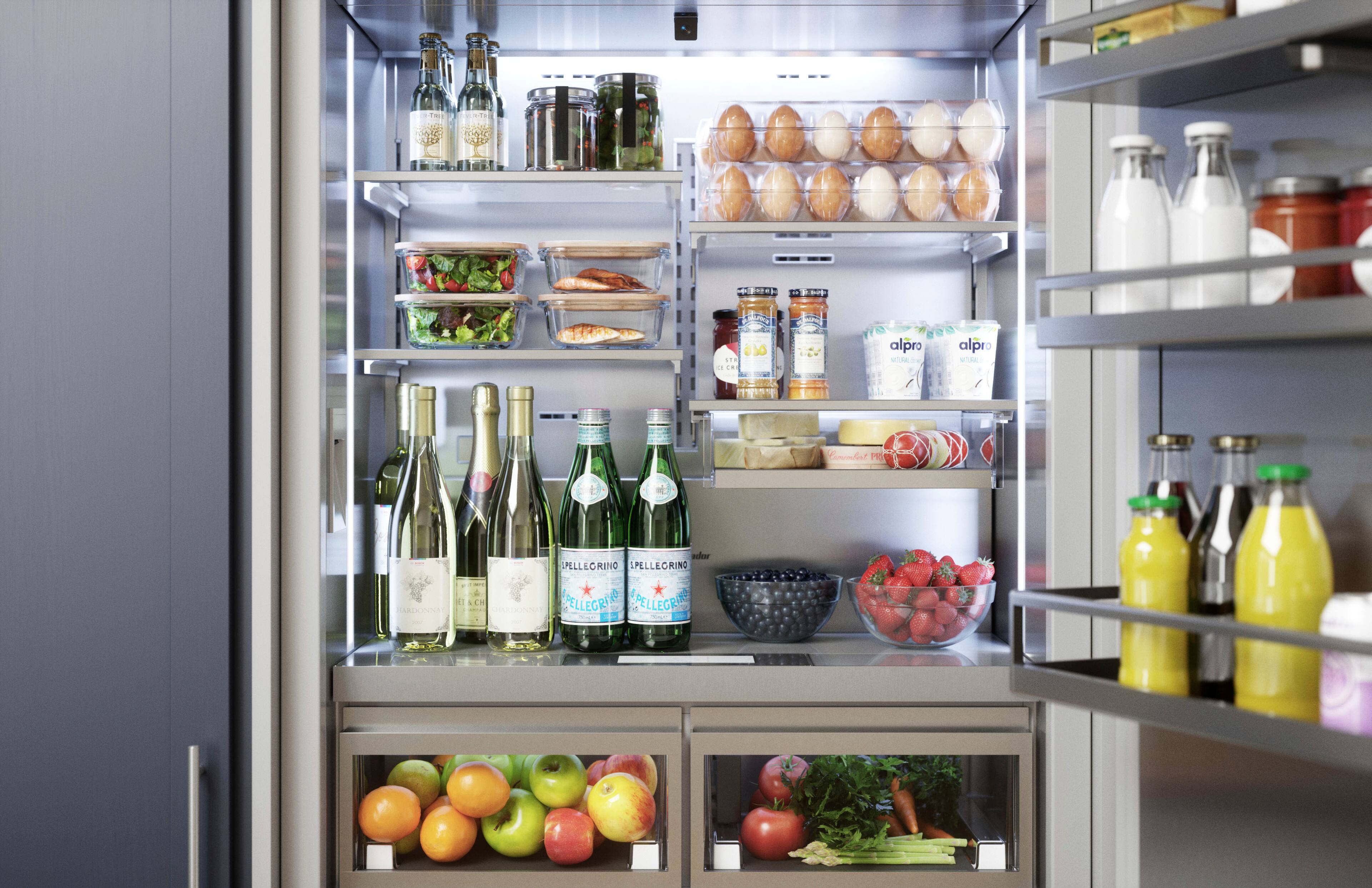 The image shows a refrigerator filled with a variety of food and drinks. There are several bottles of wine and other beverages, as well as a bowl of fruit, including apples and oranges. The refrigerator also contains a variety of other food items, such as eggs and broccoli. The refrigerator is well-stocked and offers a diverse selection of items for consumption.