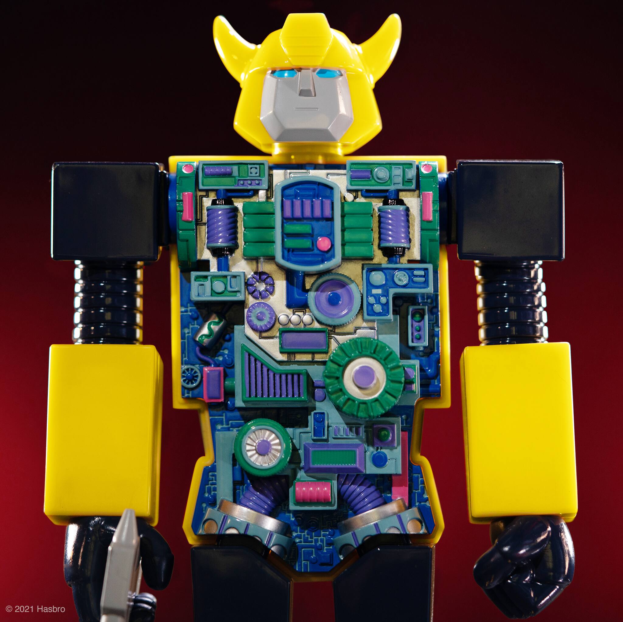 The image features a large robot action figure with a yellow head and a variety of gears and parts. The robot is standing on a red background, and it appears to be a toy or a model. The figure is intricately designed, showcasing the details of the robot's components. The robot's head is prominently displayed, and the overall scene is visually appealing, likely attracting the attention of action figure enthusiasts and collectors.