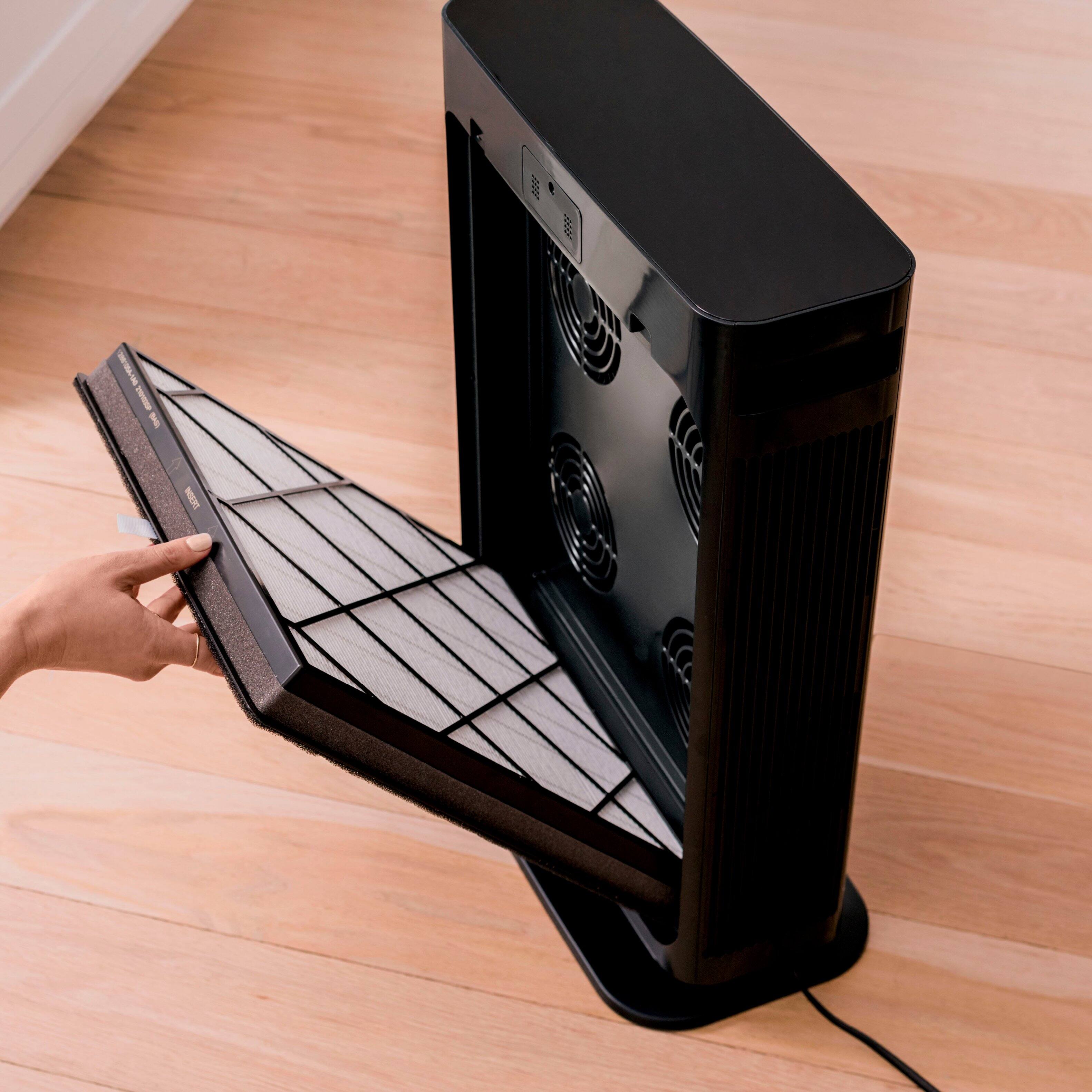 The image shows a person holding a fan with a filter attached to it. The fan is placed on a wooden floor, and the person is in the process of changing the filter. The filter is designed to deliver up to 12 months of purification, and the filter life light pulses to indicate when it's time to change the filters. This easy change filter feature makes it convenient for users to maintain clean air in their living spaces.