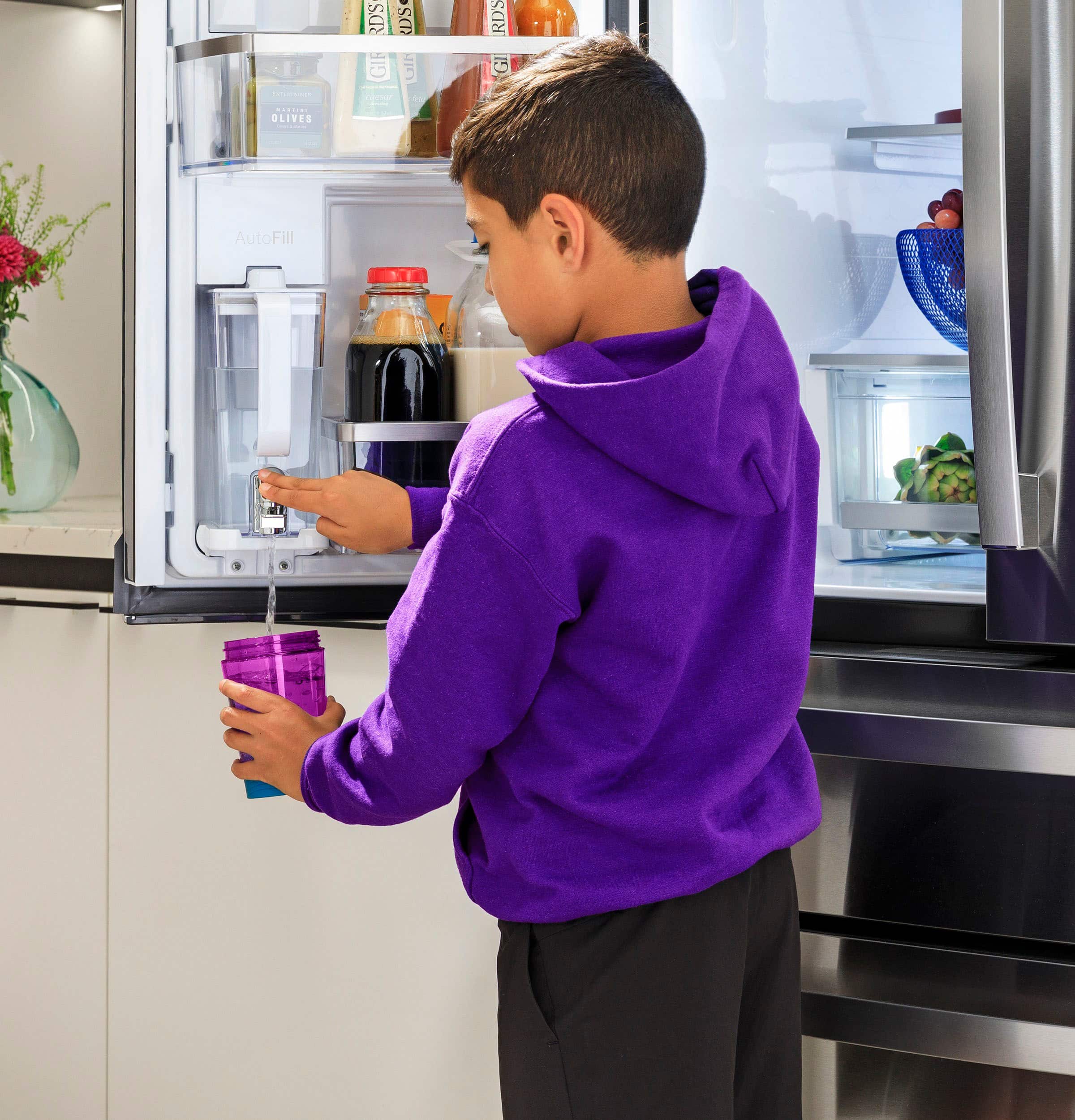 The image features a person holding a cell phone in front of a large refrigerator. The phone is open to an app, likely the SmartHQ app, which allows the user to enable Turbo Cool and Turbo Freeze settings for the refrigerator. The app also offers various options for temperature settings, water dispenser tracking, and energy consumption tracking. The person is using the app to control and manage the refrigerator's features, making it a convenient and eco-friendly way to operate the appliance.