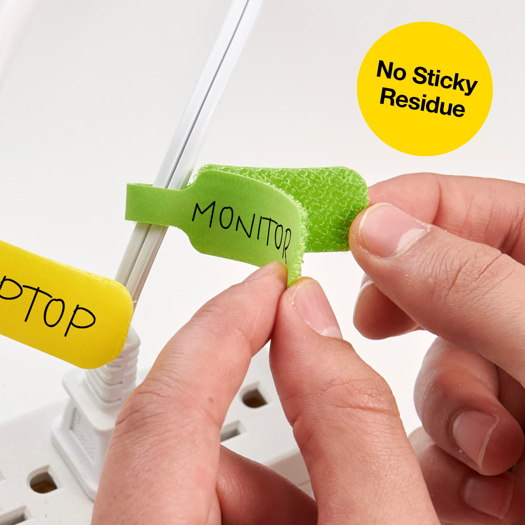 The image shows a person holding a green clip with the word "monitor" written on it. The clip is being used to secure a laptop to a monitor, ensuring that the laptop's screen is at the right height and angle for comfortable viewing. The person is using the clip to attach the laptop to the monitor, making it a convenient and practical solution for a workspace setup.