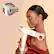 The image features a woman holding a hair dryer, which is part of the RapidGloss Finisher. This product is designed to help users achieve a naturally shiny finish by taking on frizz and flyaways. The woman in the image is wearing a red dress, and she is smiling while holding the hair dryer.