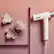 The image features a pink background with a white hair dryer and a brush. The hair dryer is placed on the left side of the image, while the brush is positioned on the right side. The focus of the image is on the hair dryer and the brush, which are both essential tools for styling and maintaining hair. The pink background adds a pop of color to the scene, making it visually appealing.