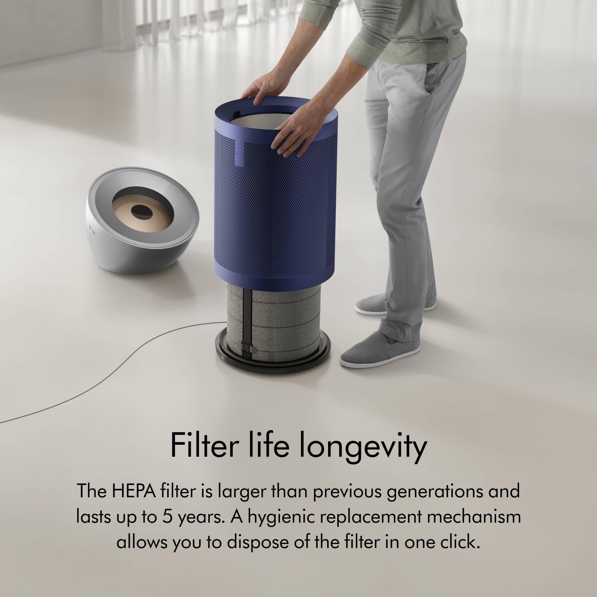 The image features a man standing next to a blue and silver air purifier. The main focus of the image is the HEPA filter, which is larger than previous generations and lasts up to 5 years. The hygienic replacement mechanism allows for easy disposal of the filter in just one click. The man's presence in the image suggests that he is either using the air purifier or demonstrating its features.