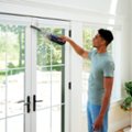 The image features a man standing in front of a sliding glass door, holding a handheld vacuum cleaner. The man is using the vacuum to clean the glass door, which is a part of a sliding glass door system. The handheld vacuum is compact, lightweight, and powerful, making it an efficient tool for cleaning tasks.