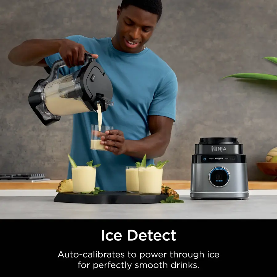 The image features a man pouring a smoothie into a glass, with a Ninja blender in the background. The Ninja blender is designed to auto-calibrate to power through ice for perfectly smooth drinks. The man is standing next to the blender, which is placed on a counter. The scene also includes a potted plant and a bowl, adding to the overall atmosphere of the kitchen setting.