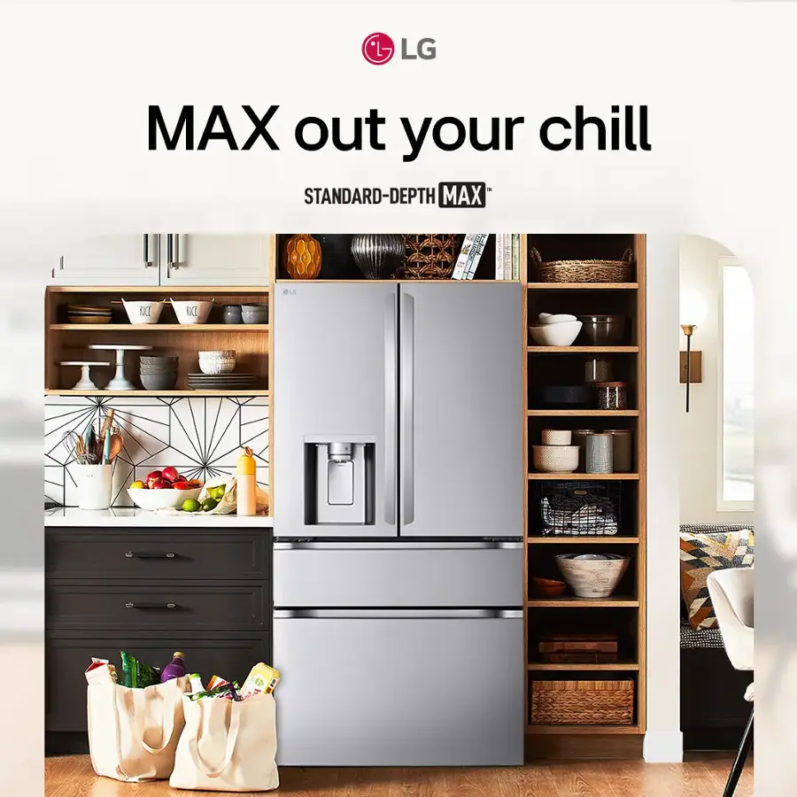 The image showcases a kitchen with a large gray refrigerator freezer, which is the main focus of the scene. The refrigerator is positioned in the middle of the kitchen, surrounded by various items such as bowls, cups, and bottles. There are also several apples and oranges placed around the kitchen, adding a touch of color to the scene.

In the background, there is a dining table with chairs, and a book can be seen on the table. The kitchen appears to be well-organized and functional, with the refrigerator being the centerpiece of the space.