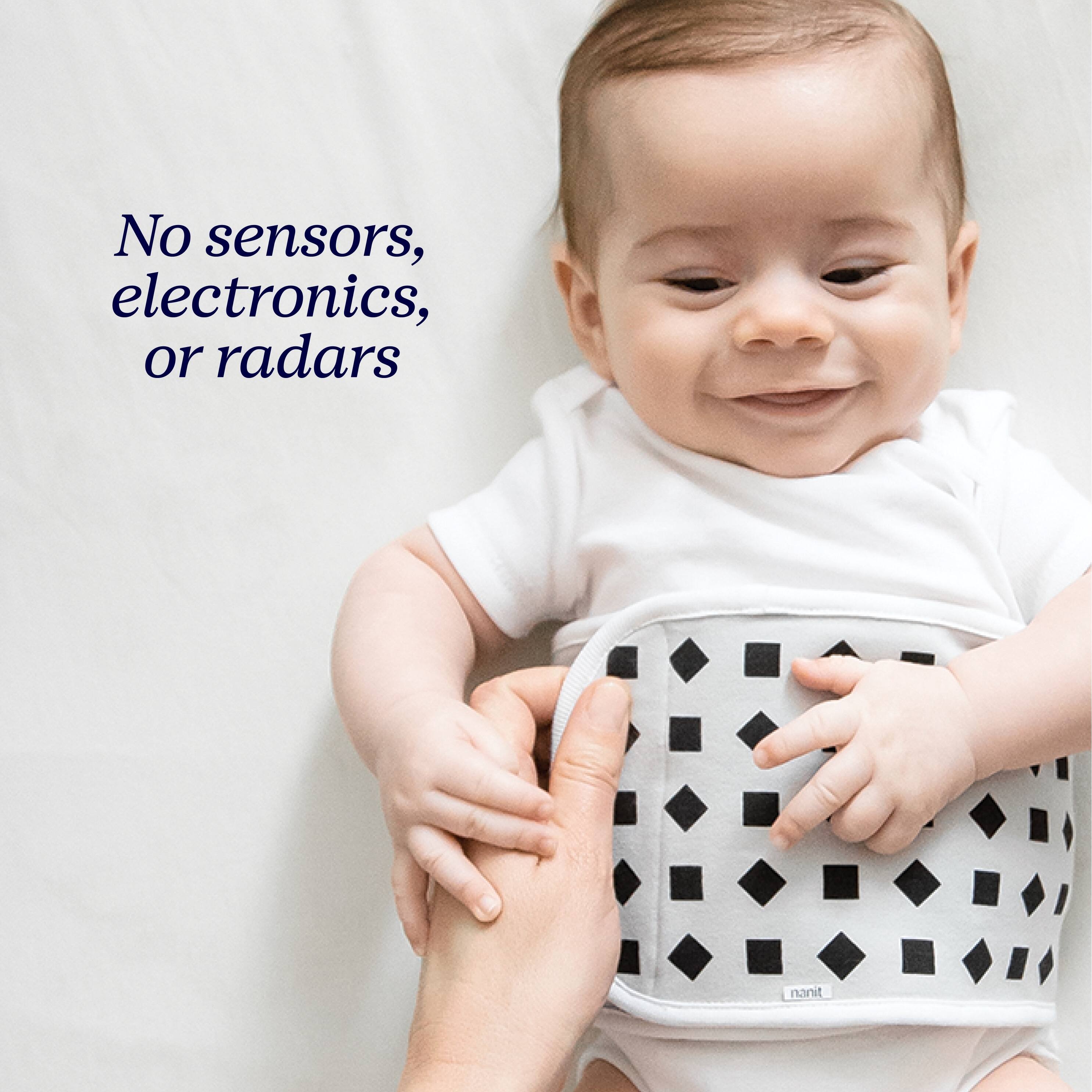 The image features a baby wearing a white onesie and smiling. The baby is being held by an adult, and the baby is wearing a white and black polka dot diaper. The focus of the image is on the baby and the interaction between the baby and the adult, rather than on any baby monitoring devices.
