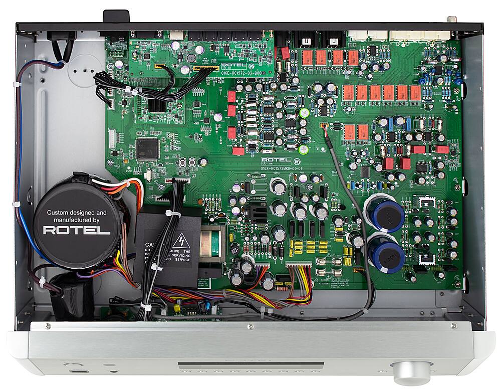 The image features a close-up of a ROTEL electronic device, specifically a custom designed and manufactured piece of equipment. The device is made up of various components, including a green circuit board and a power supply. The circuit board is filled with numerous wires and connections, showcasing the intricate design and construction of the device. The power supply is located on the left side of the circuit board, and the device is likely used for a range of applications, such as audio or video processing.