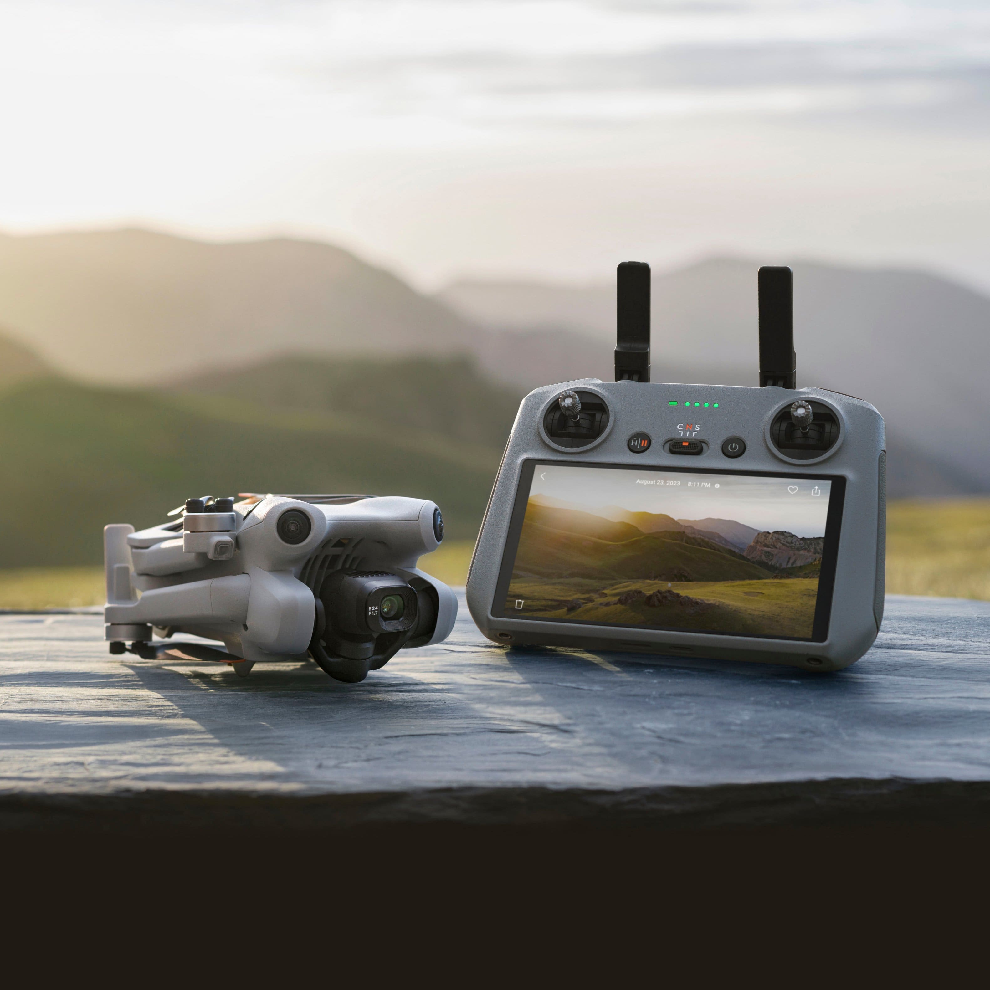 The image features a drone with a camera attached to it, sitting on a rocky surface. The drone is equipped with a remote control, allowing for easy operation. The scene is set against a backdrop of mountains, creating a picturesque and adventurous atmosphere.