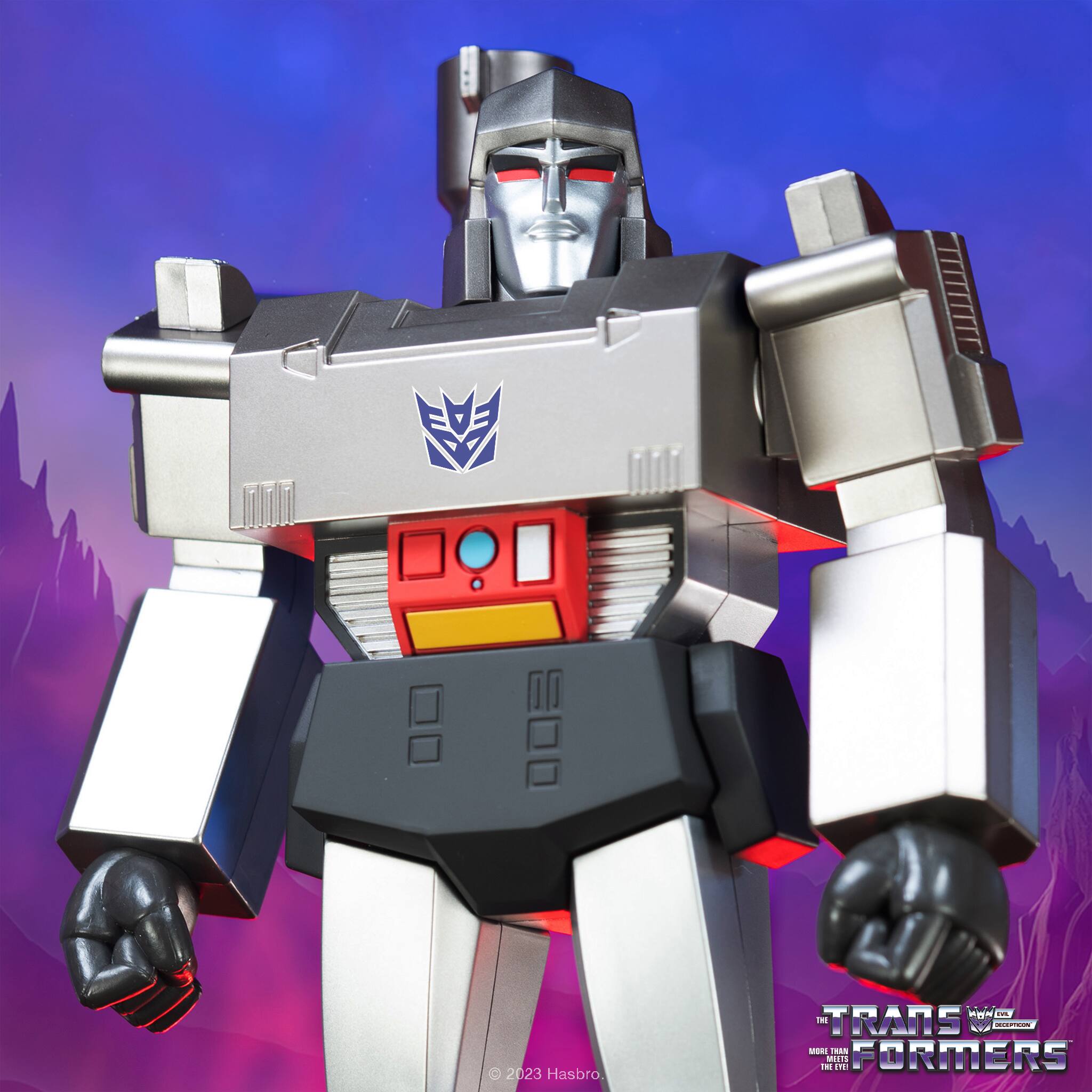 The image features a robot action figure, possibly a Transformer, standing in a dark room. The robot has a silver and black color scheme, and it appears to be a toy. The figure is prominently displayed in the foreground, with a mountain visible in the background.