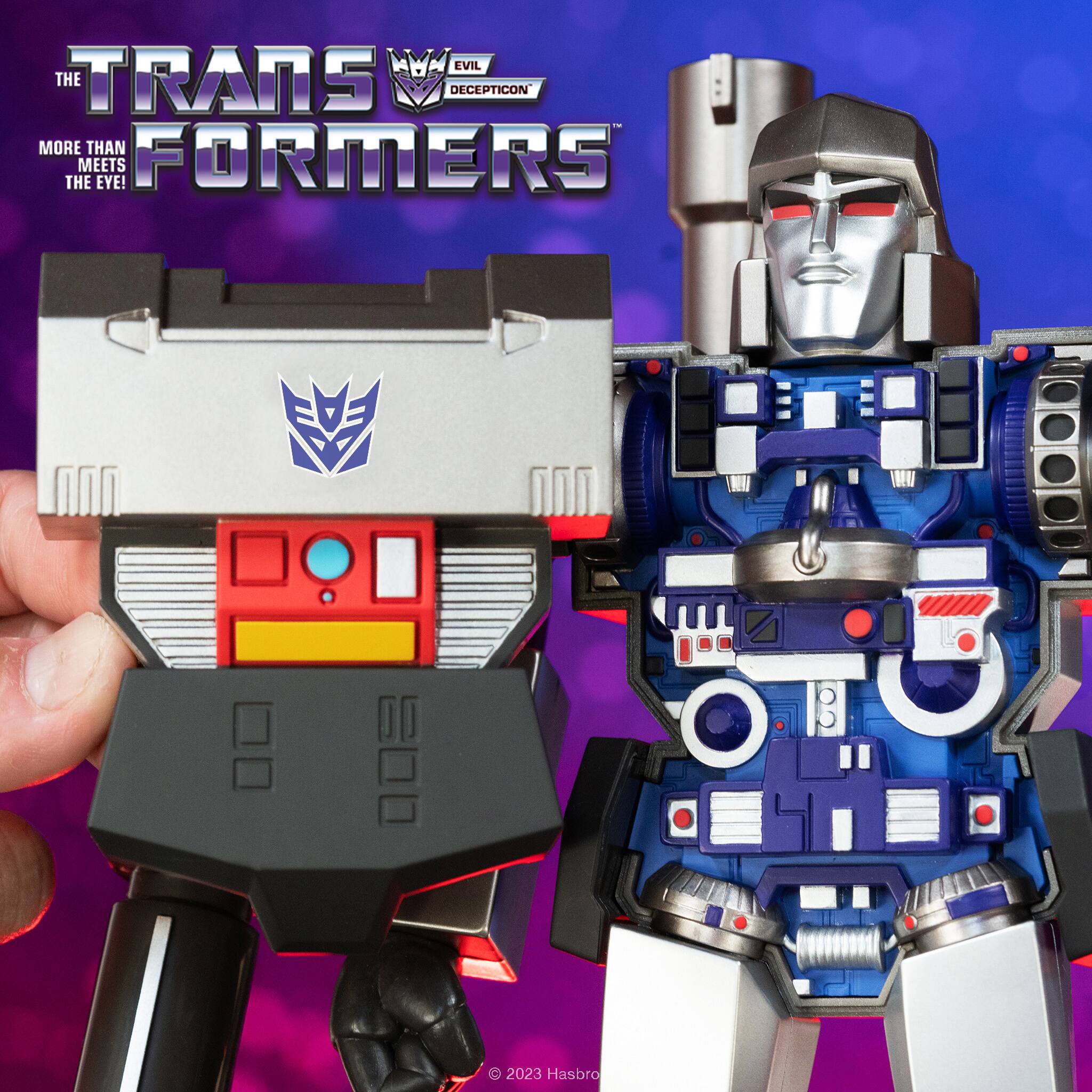 The image features a person holding a toy robot, which is a part of the Transformers franchise. The robot is a large, metallic figure with a distinctive red and blue color scheme. The toy is designed to resemble a robotic character from the Transformers universe. The person holding the robot is likely a fan or collector of Transformers action figures.