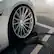 The image shows a white car with a black tire and a black cord plugged into it. The car is parked in a parking lot, and the cord is connected to a charger. The car is likely being charged or recharged, as indicated by the presence of the cord and charger.