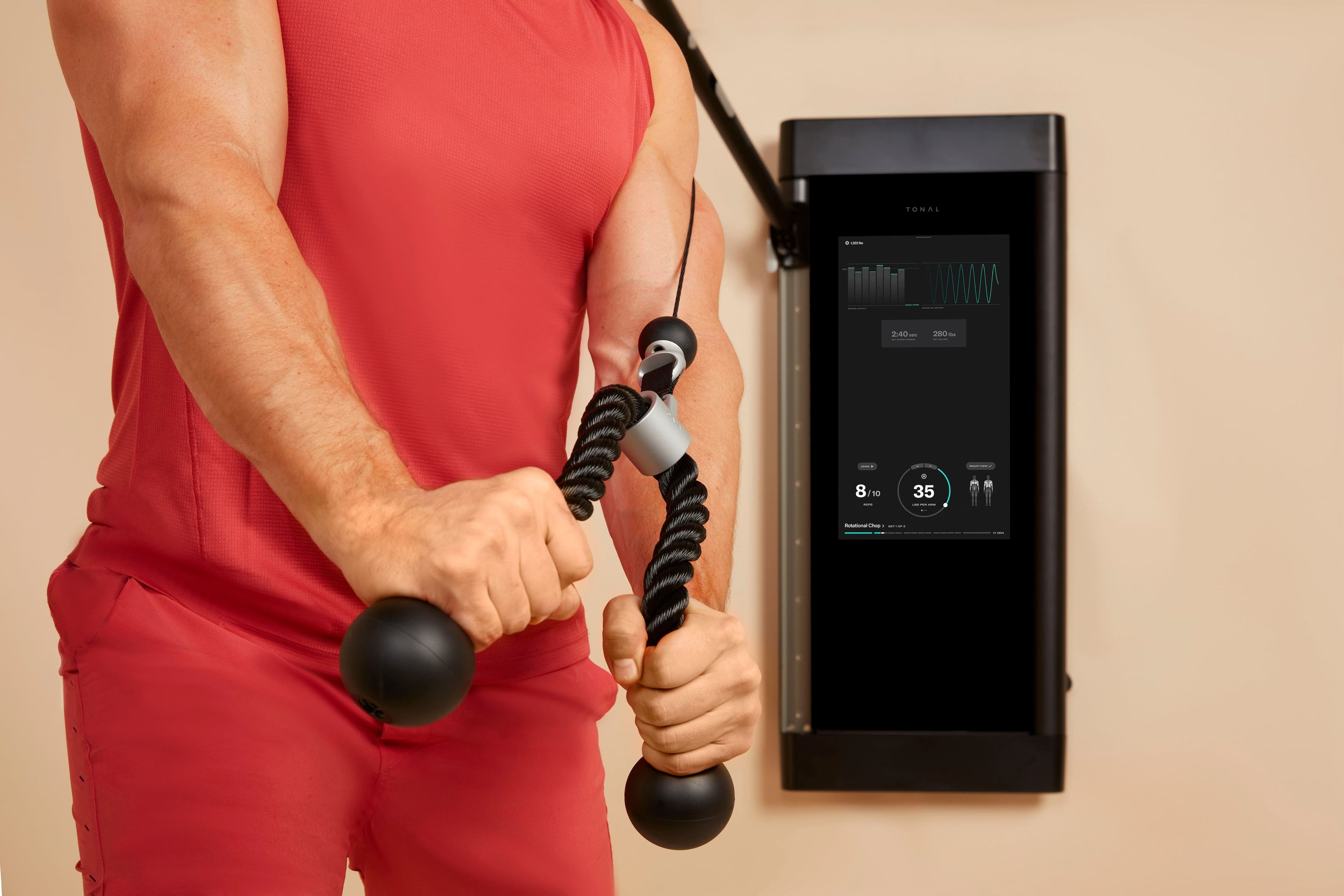 The image shows a man wearing red pants and a red shirt, holding a weight in each hand. He is standing in front of a machine, possibly a weight machine or a resistance device. The man is engaging in a workout, possibly using the machine to improve his strength and fitness. The machine has a display, which might show the man's progress or provide instructions for the exercise.