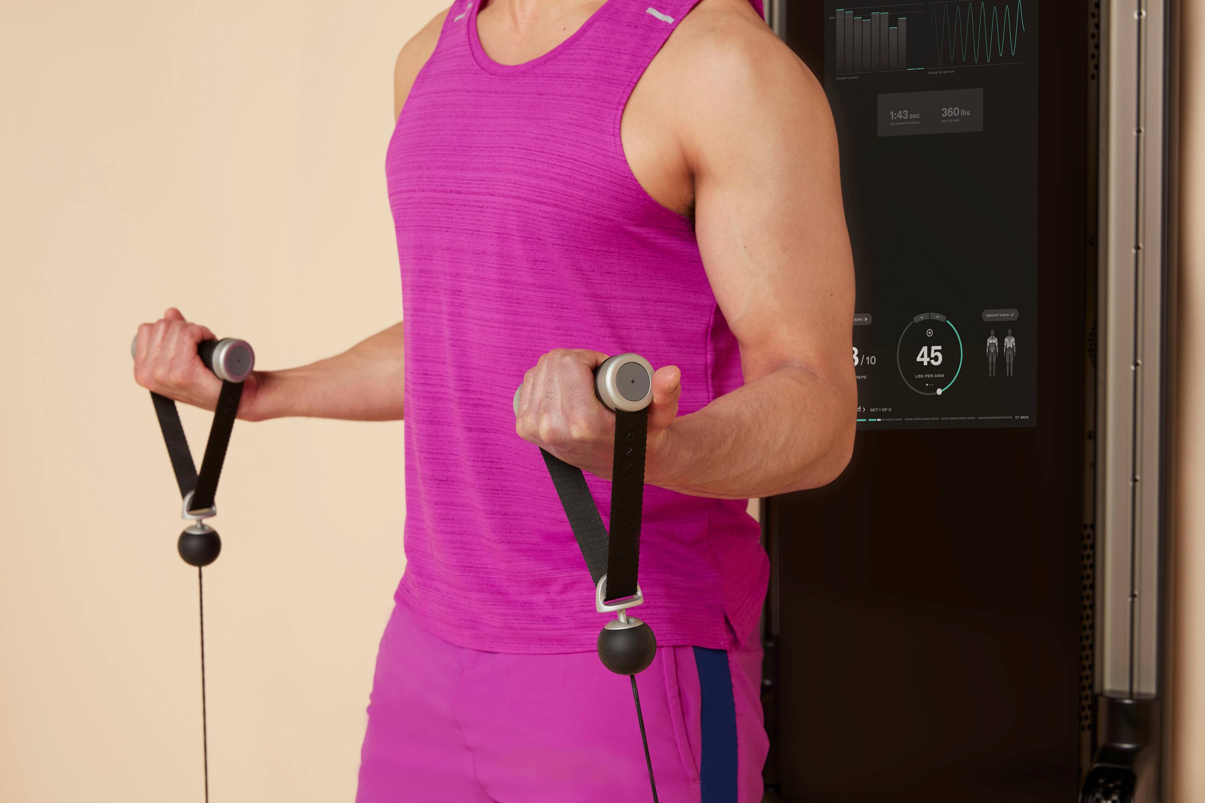 The man is wearing a pink shirt and holding onto a resistance band. He is standing in front of a machine, which displays the time 1:43. The resistance band is attached to the machine, possibly for a workout or exercise routine.