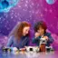 The image shows a boy and a girl sitting at a table, building a Lego space shuttle together. They are surrounded by various Lego pieces, including a truck and a car. The girl is on the left side of the table, while the boy is on the right. They are both focused on their project, enjoying their time together.