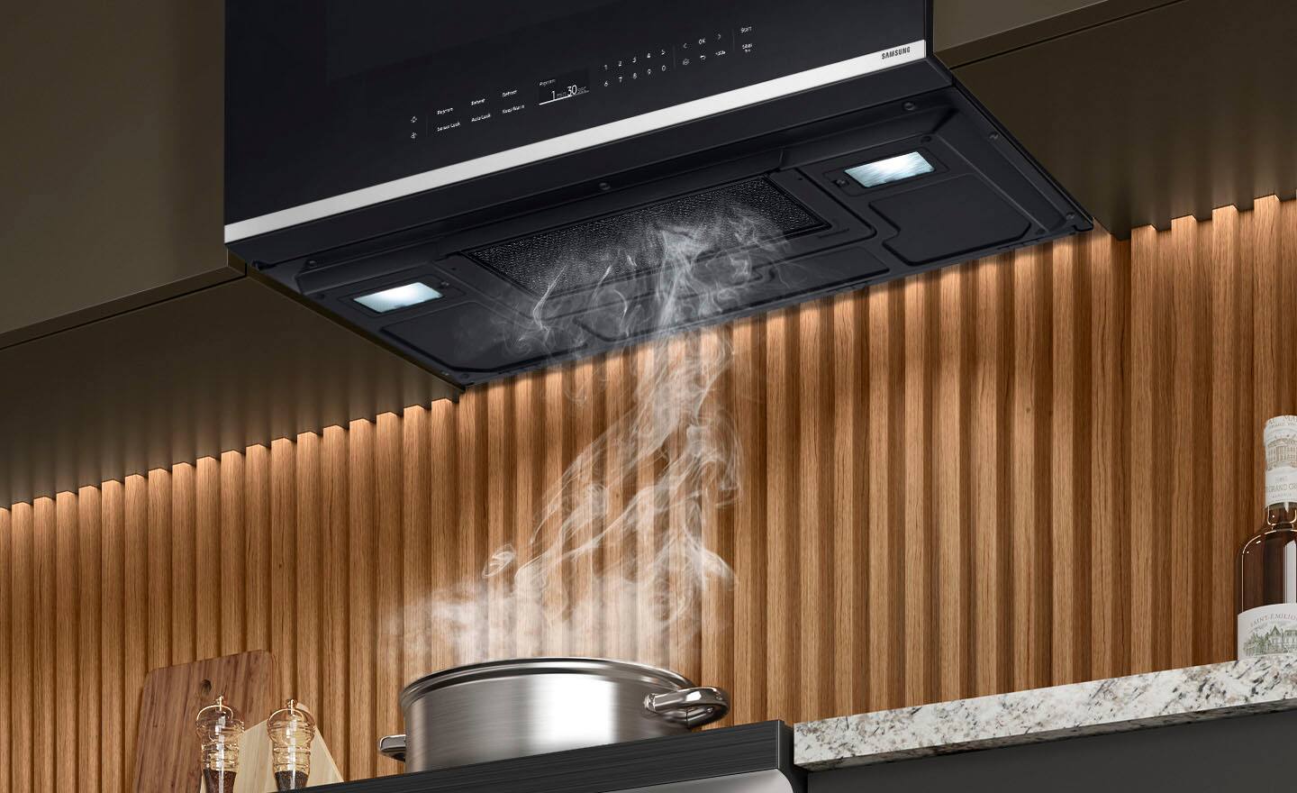 The image shows a kitchen scene with a pot on the stove, and steam is rising from the pot. The stove is a Samsung Grand C Emilio model. The kitchen also features a microwave and a sink. There are several bottles on the countertop, and a bowl is placed nearby. The overall setting appears to be a modern and well-equipped kitchen.