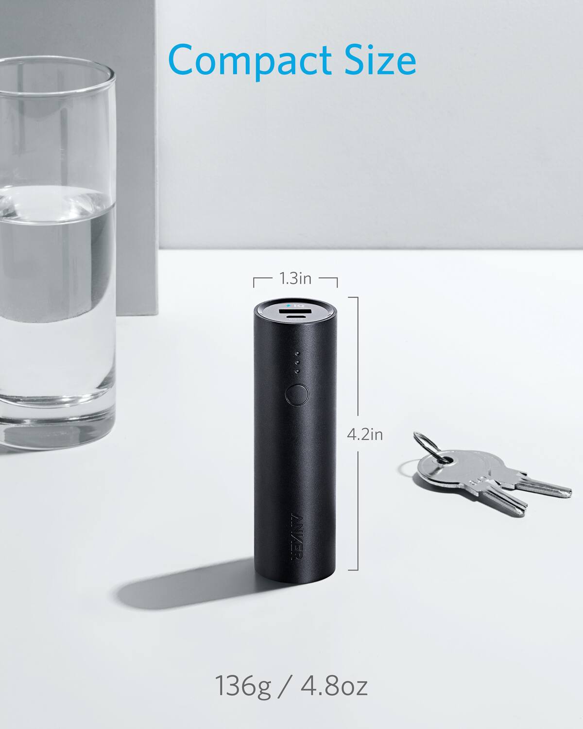 The image features a compact size portable power pack, which is a product by Anker. The power pack is displayed on a white surface, and it is accompanied by a set of keys. The dimensions of the power pack are 1.3 inches by 4.2 inches, and it weighs 136 grams or 4.8 ounces.