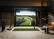 The image shows a large screen with a golf course displayed on it. The screen is placed in a room with a couch and a chair nearby. There is also a golf club and a remote control in the room. The scene suggests that this is a golf simulator, allowing people to play golf indoors.