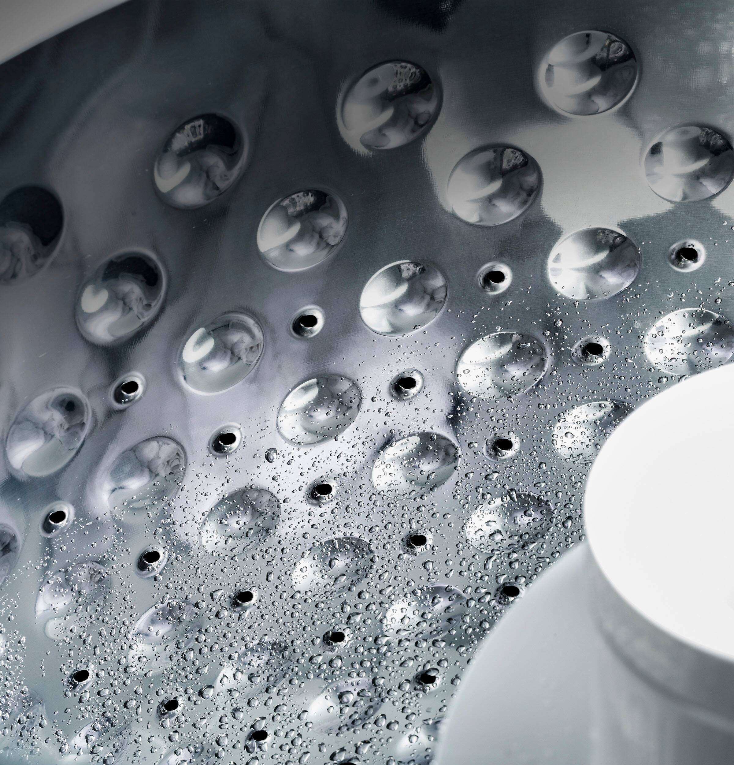 The image features a silver shower head with a pattern of holes on it. The shower head is positioned above a sink, and it appears to be covered in water droplets. The droplets are scattered across the shower head, giving it a shiny appearance. The sink is located to the right of the shower head, and the overall scene creates an impression of a well-maintained bathroom.