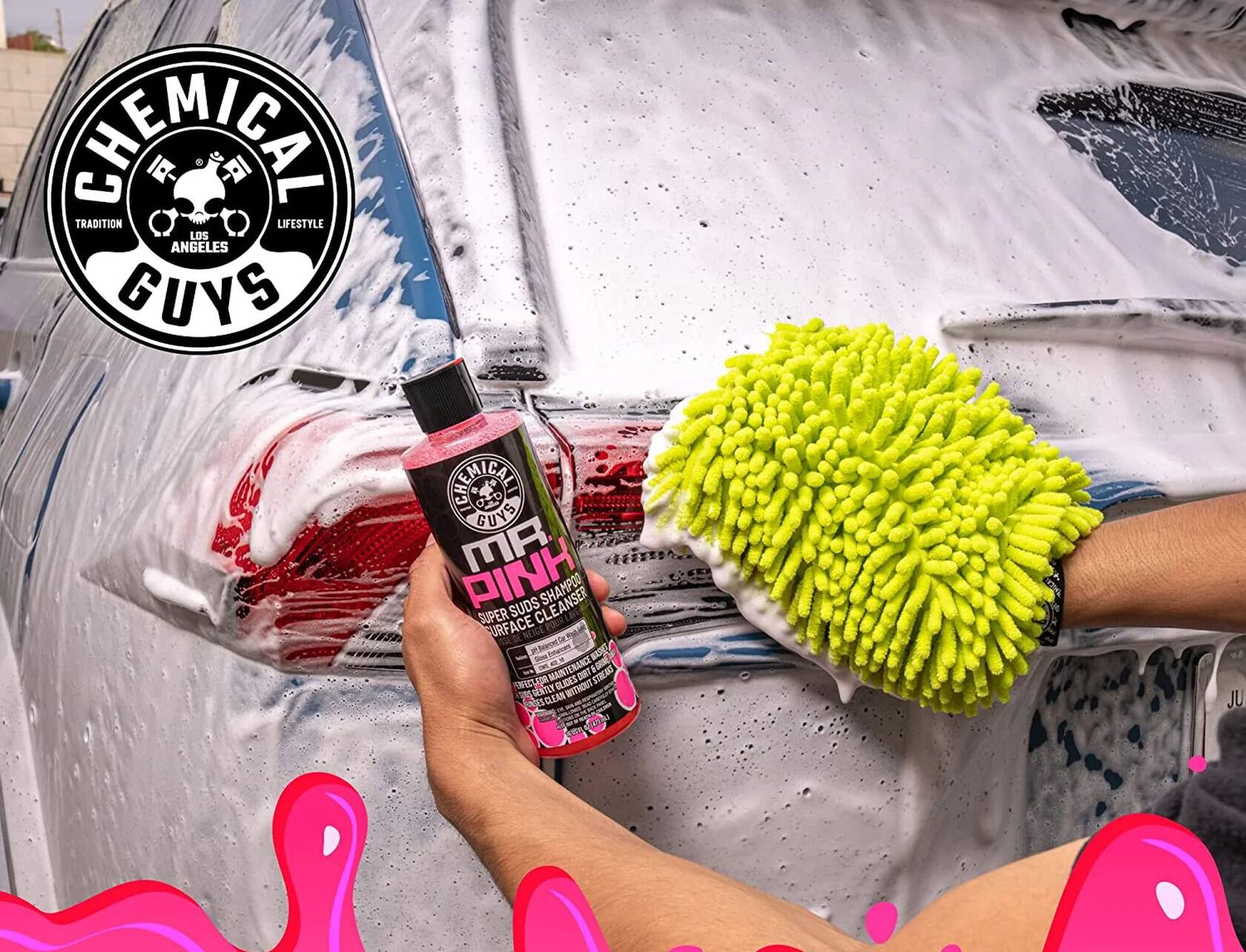 The image features a person using a sponge and a bottle of pink cleaner to clean a car. The car is being sprayed with the cleaner, and the person is holding the sponge to apply the cleaner to the car's surface. The scene is set against a backdrop of a car wash, with a car being washed in the background. The image is part of a larger advertisement for a car cleaning solution, showcasing the effectiveness of the product in cleaning vehicles.