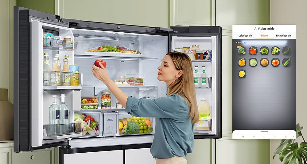 The image features a woman standing in front of a large refrigerator, which is categorized as a Full_Size_Refrigerator. The refrigerator has a large screen on its door, which is likely used for displaying information or advertisements. The woman is holding an apple and appears to be looking at the contents of the refrigerator. The refrigerator is filled with various food items, including several bottles, a bowl, and a potted plant.
