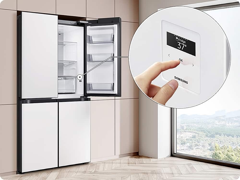 The image shows a kitchen with a refrigerator and a window. The refrigerator is white and has a digital display on the front. A hand is seen pressing a button on the display, possibly adjusting the temperature or selecting a specific setting. The refrigerator is a Samsung model, as indicated by the brand name displayed on the front.