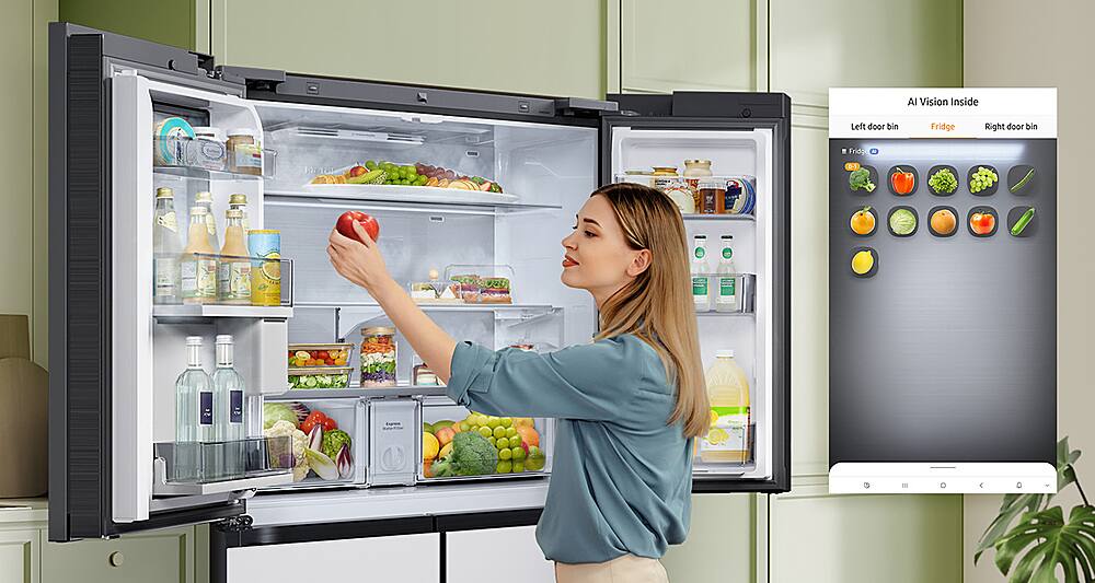 The image features a woman standing in front of a large refrigerator, which is categorized as a Full_Size_Refrigerator. The refrigerator has a large screen on its door, which is likely used for displaying information or advertisements. The woman is holding an apple and appears to be looking at the contents of the refrigerator. The refrigerator is filled with various food items, including several bottles, a bowl, and a potted plant.