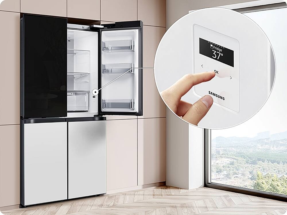 The image shows a kitchen with a large refrigerator and a window. A person is holding a Samsung smart device, which is placed on the refrigerator. The device is likely used to control the refrigerator's temperature or other settings. The refrigerator is empty, and the kitchen appears to be well-maintained and organized.