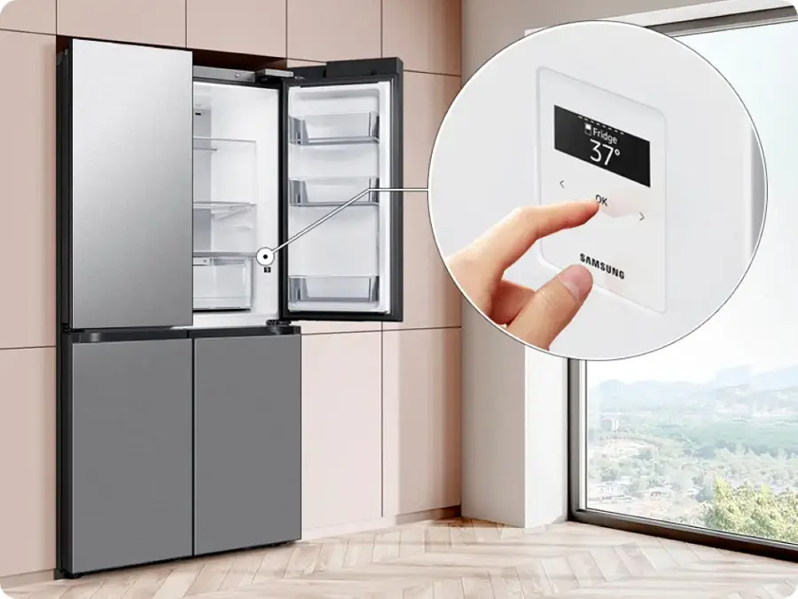 The image shows a kitchen scene with a refrigerator and a freezer. A person is holding a remote control in front of the refrigerator, likely adjusting the temperature or settings. The refrigerator and freezer are both made by Samsung, as indicated by the visible brand name.