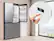 The image shows a kitchen scene with a refrigerator and a freezer. A person is holding a remote control in front of the refrigerator, likely adjusting the temperature or settings. The refrigerator and freezer are both made by Samsung, as indicated by the visible brand name.