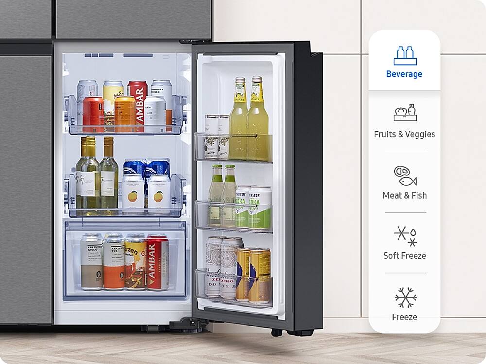 The image shows a refrigerator with its door open, revealing a variety of drinks and food items. There are multiple bottles of beverages, including water, juice, and soda, as well as a few cans of soda. The refrigerator also contains a few fruits, such as apples and oranges. The refrigerator is equipped with a freezer and a soft freeze feature, which allows for easy access to frozen items. The refrigerator is a part of a larger kitchen setup, with a sink and a microwave nearby.