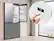 The image shows a kitchen scene with a refrigerator and a freezer. A person is holding a remote control in front of the refrigerator, likely adjusting the temperature or settings. The refrigerator and freezer are both made by Samsung, as indicated by the visible brand name.