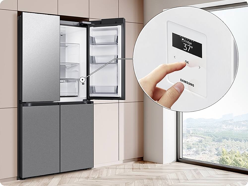 The image shows a kitchen scene with a refrigerator and a freezer. A person is holding a remote control in front of the refrigerator, likely adjusting the temperature or settings. The refrigerator and freezer are both made by Samsung, as indicated by the visible brand name.