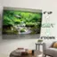 The image features a large flat screen TV mounted on the wall. The TV is turned on and displaying a scene of a stream with rocks. There is a couch in the room, and a potted plant is placed nearby. The TV is described as having a 4" up shift and 4" down shift, which likely refers to the adjustable screen height or angle.