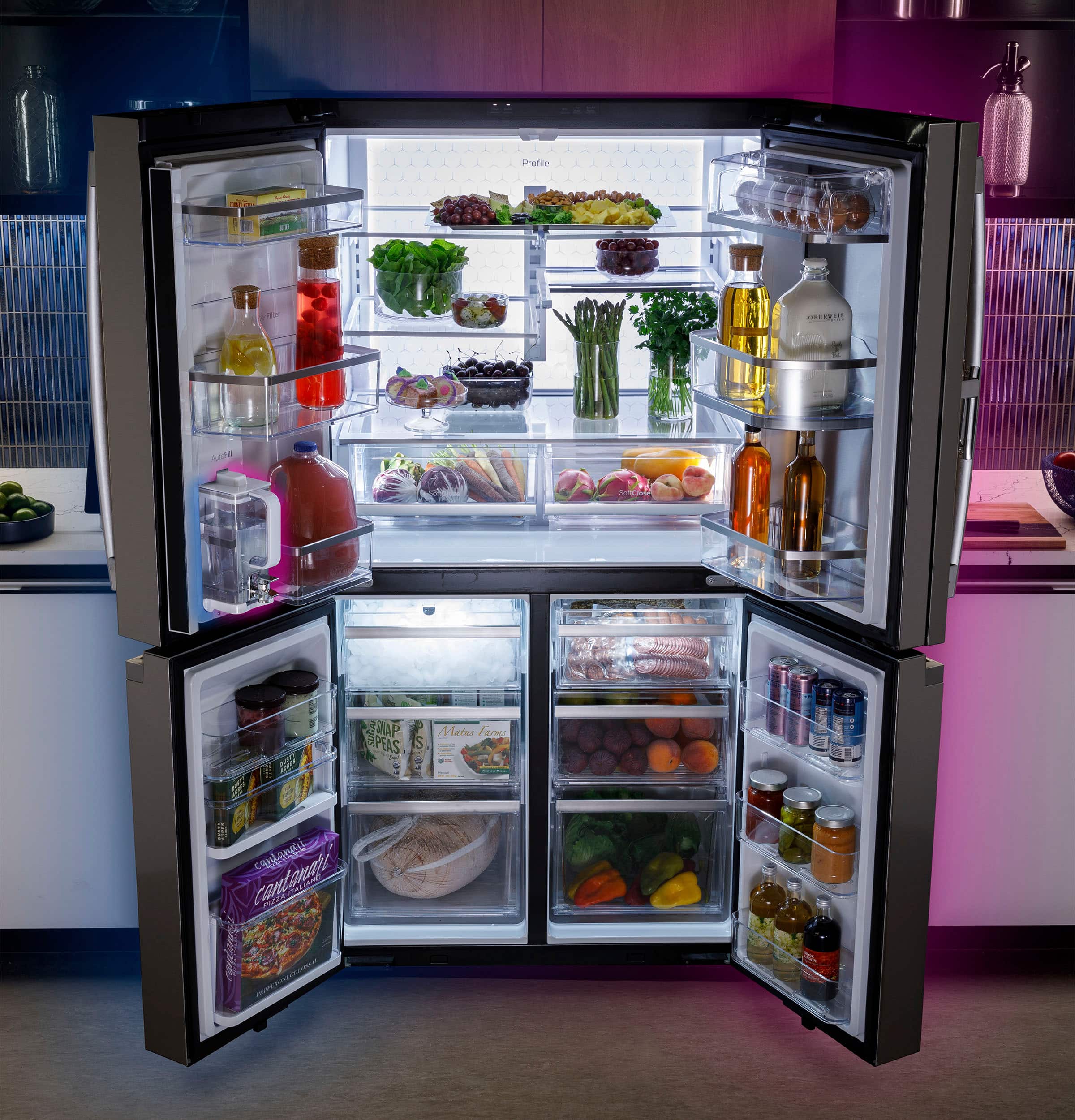The image features a large refrigerator with its door open, revealing a well-stocked interior. The refrigerator is filled with a variety of food items, including fruits, vegetables, and bottles. There are multiple apples, oranges, and carrots visible inside the refrigerator, as well as several bottles placed in different compartments. The refrigerator is well-organized, with the food items neatly arranged to make it easy to find and access what is needed.