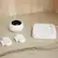 The image shows a white Arlo device, which is a smart home security system, sitting on a countertop. The Arlo device is accompanied by two white Arlo remotes, which are used to control the device. The remotes are placed next to the Arlo device, and the entire setup is displayed on a white marble countertop.